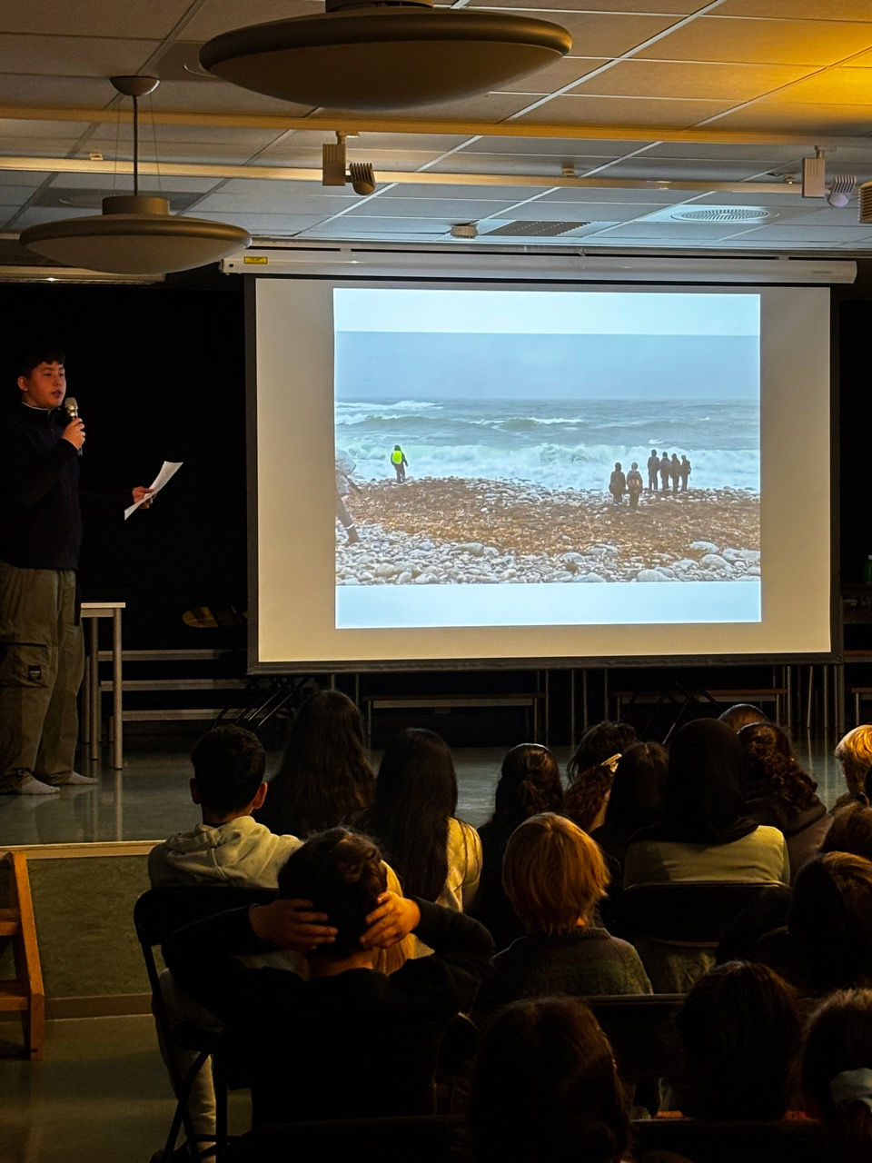 en person som snakker til en gruppe mennesker i et rom med en stor skjerm