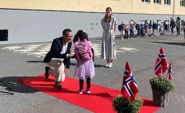 en person og en person som sitter på en rød løper foran en bygning med mennesker som står og