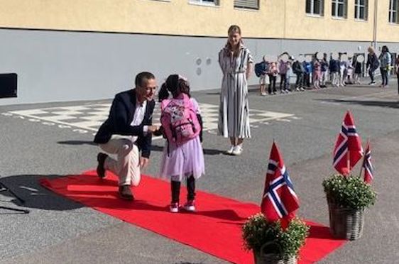 en person og en person som sitter på en rød løper foran en bygning med mennesker som står og