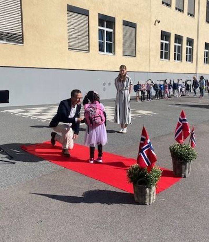 en person og en person som sitter på en rød løper foran en bygning med mennesker som står og